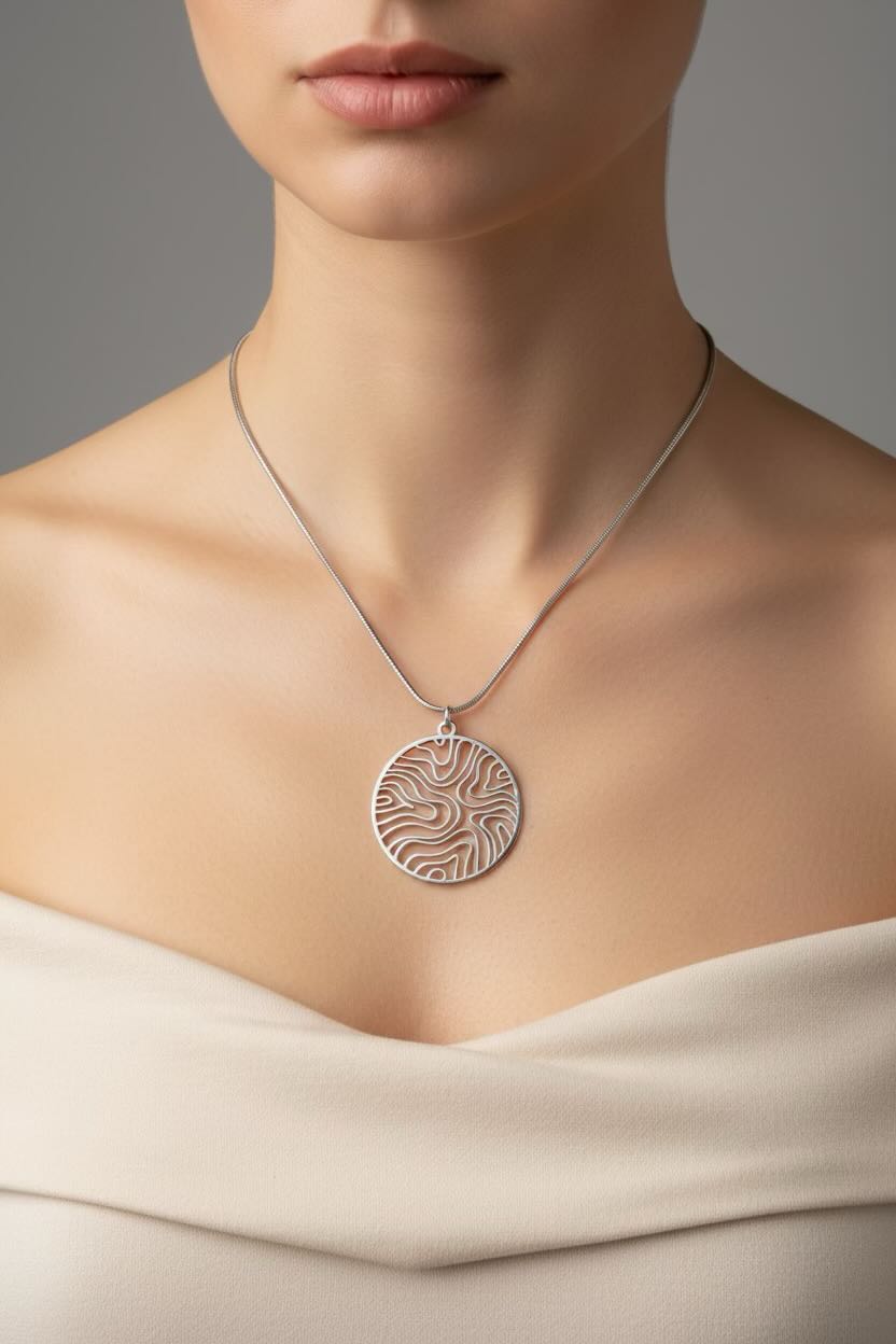 A close-up of a model wearing a silver pendant necklace with a circular, wave pattern circle patterned pendant on a delicate silver chain.