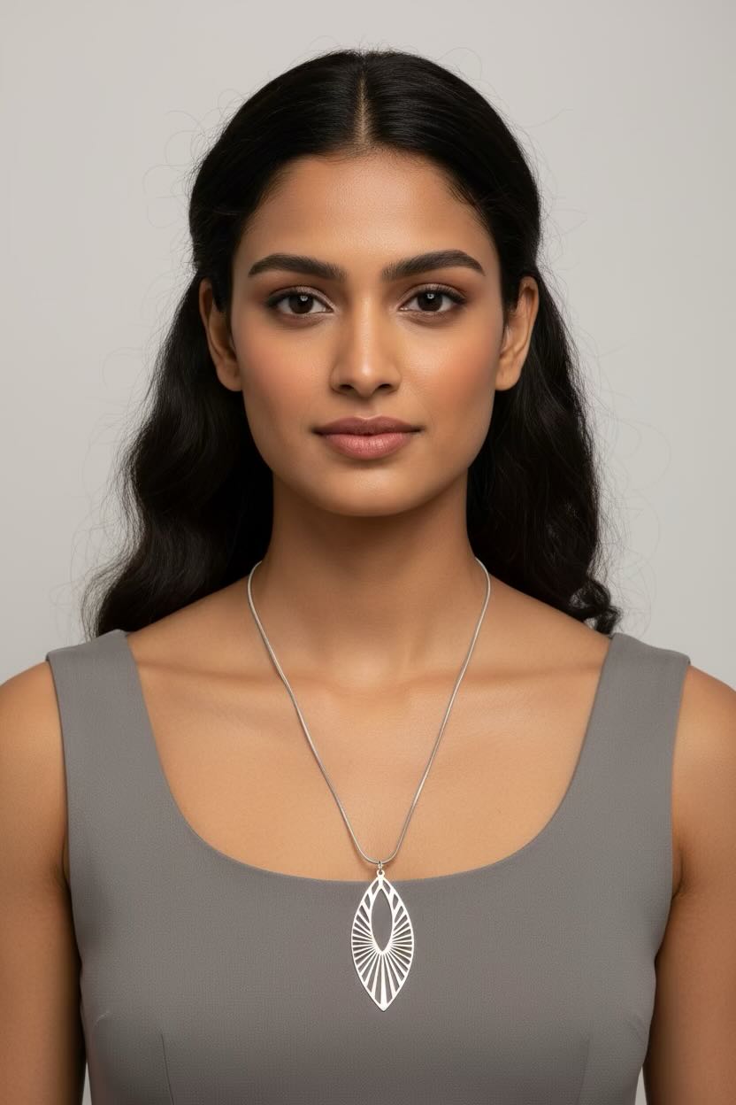 A woman with dark hair wearing a silver pendant necklace with a sunburst design, paired with a gray sleeveless top, against a neutral gray background.
