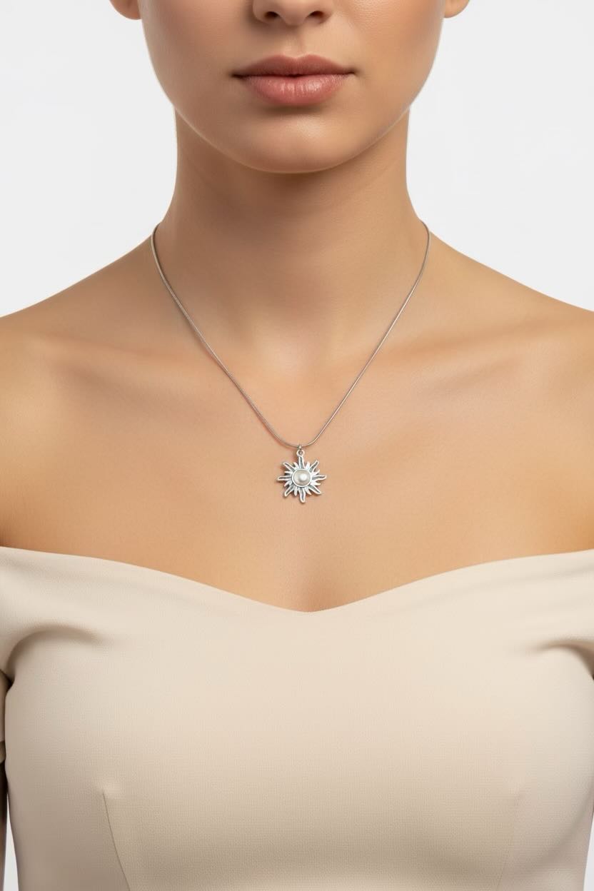 A close-up of a model wearing a delicate silver chain necklace with a starburst-shaped silver pendant, paired with a beige off-the-shoulder top against a light gray background.