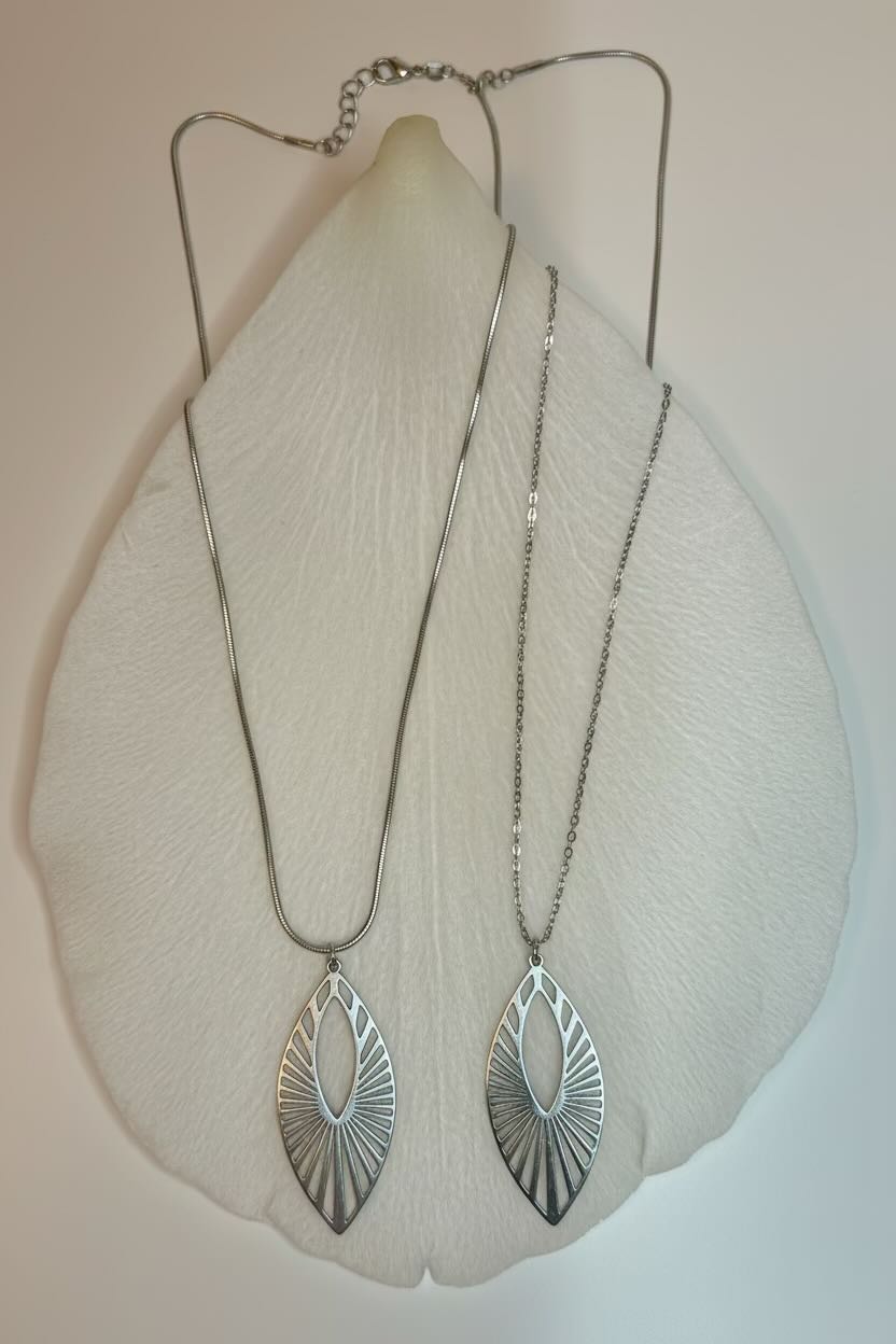 Two silver sunburst marquise-shaped pendant necklaces displayed on a white textured stand against a light beige background.