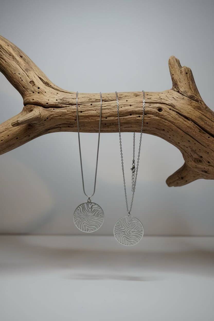 Two pendant necklaces with a circular, wave pattern circle patterned pendant hanging on a branch.