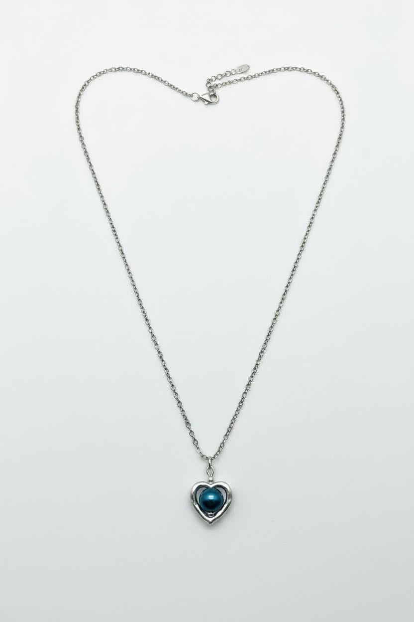 A silver chain necklace with a heart-shaped pendant featuring a steel blue iridescent center, displayed on a light gray background.