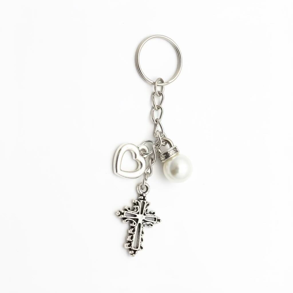 Silver-tone metal keyring/keyrings with a split key ring, dangling heart charm, textured cross charm, and a small white pearl bead, shown on a plain white background.