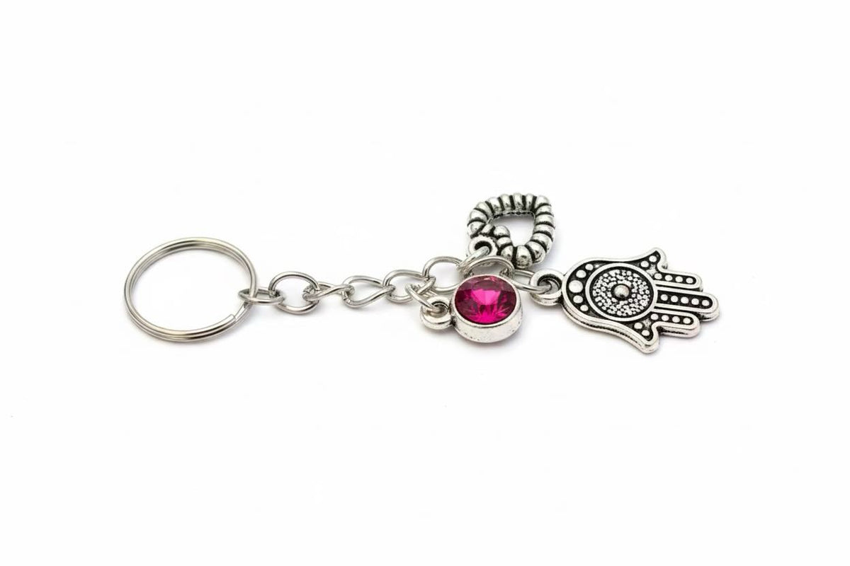 A silver-tone metal keyring/keyrings featuring a Hamsa hand charm, a lock charm, and a small round pink gemstone accent, shown on a plain white background.