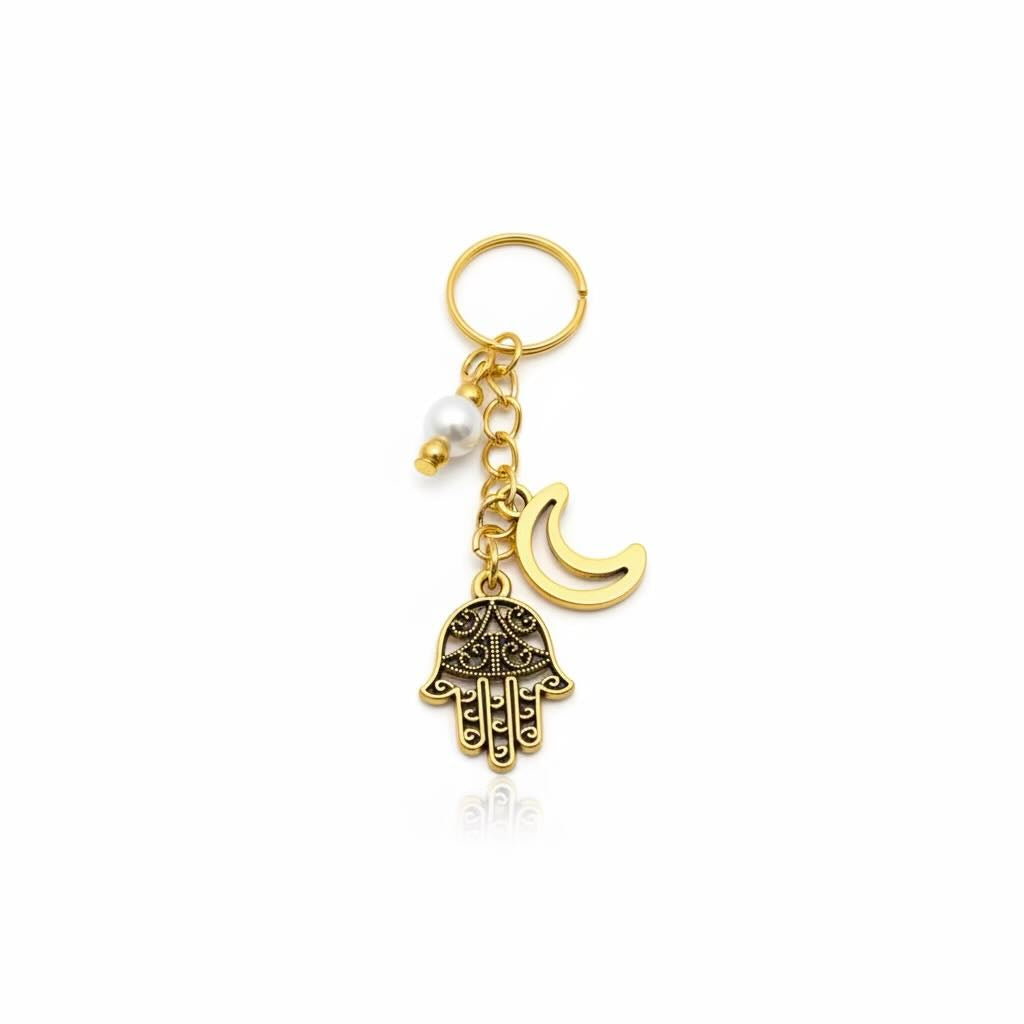 Gold-tone Hamsa hand keyring with a crescent moon charm, a small white pearl bead, and a split key ring on a white background.