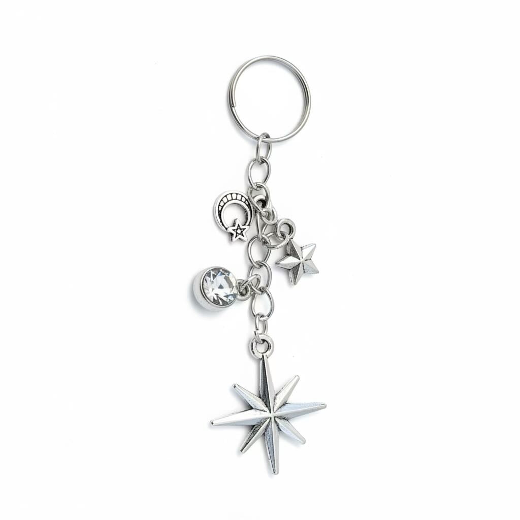 A silver-toned metal keyring/keyrings featuring a large eight-pointed North star charm, a smaller five-pointed star, a crescent moon with stars, a clear faceted gemstone, and a circular key ring, shown on a plain white background.