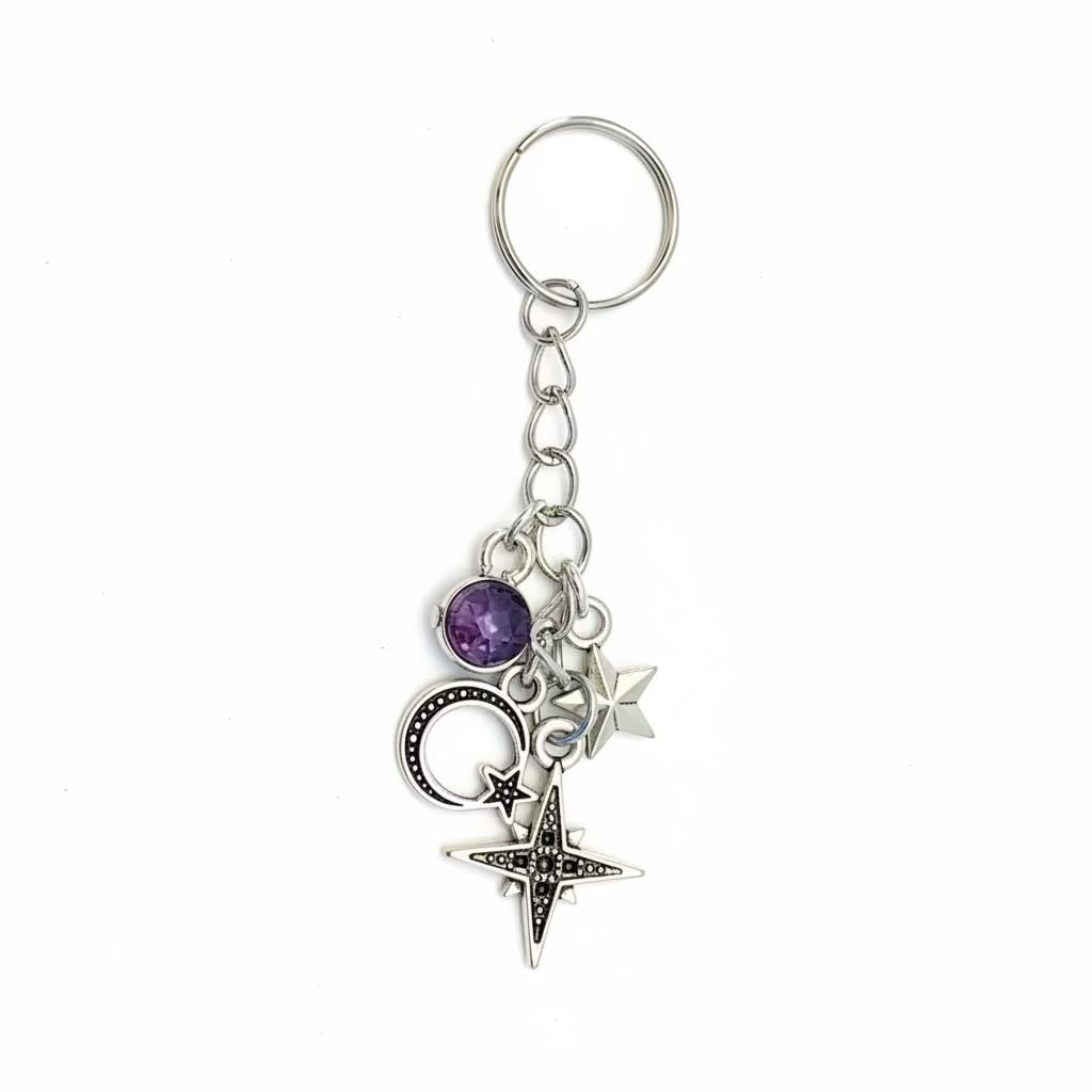 A silver-toned metal keyring/keyrings featuring a round key ring, short chain, and multiple charms including a purple faceted gemstone, a crescent moon, stars, and a compass star, shown on a plain white background.