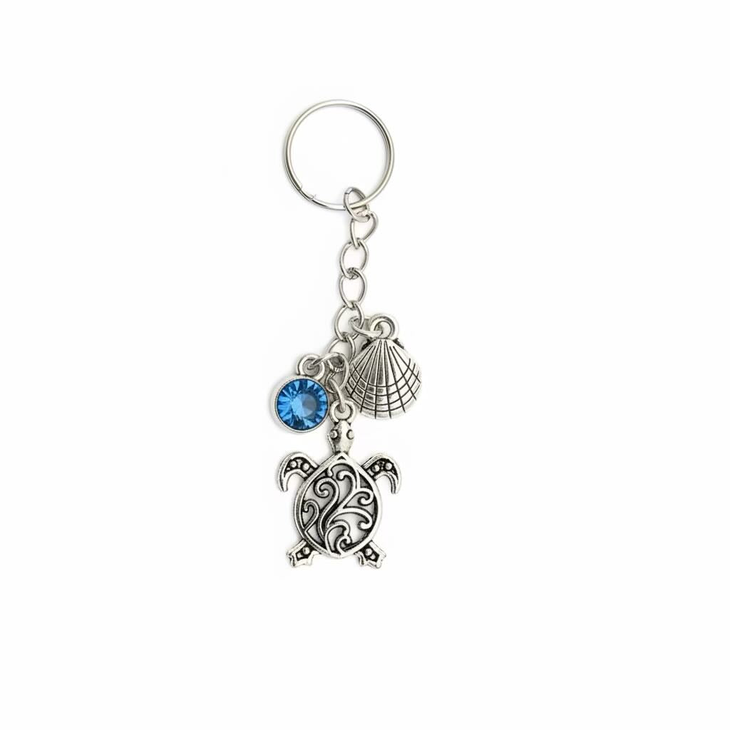 A silver-toned keyring/keyrings featuring a sea turtle charm with Maori-style tattoo patterns, a turtle charm, and a round blue crystal charm, shown on a plain white background.