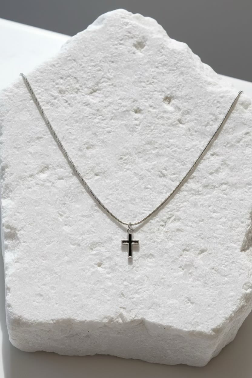Silver necklace with a cross pendant on a textured white surface