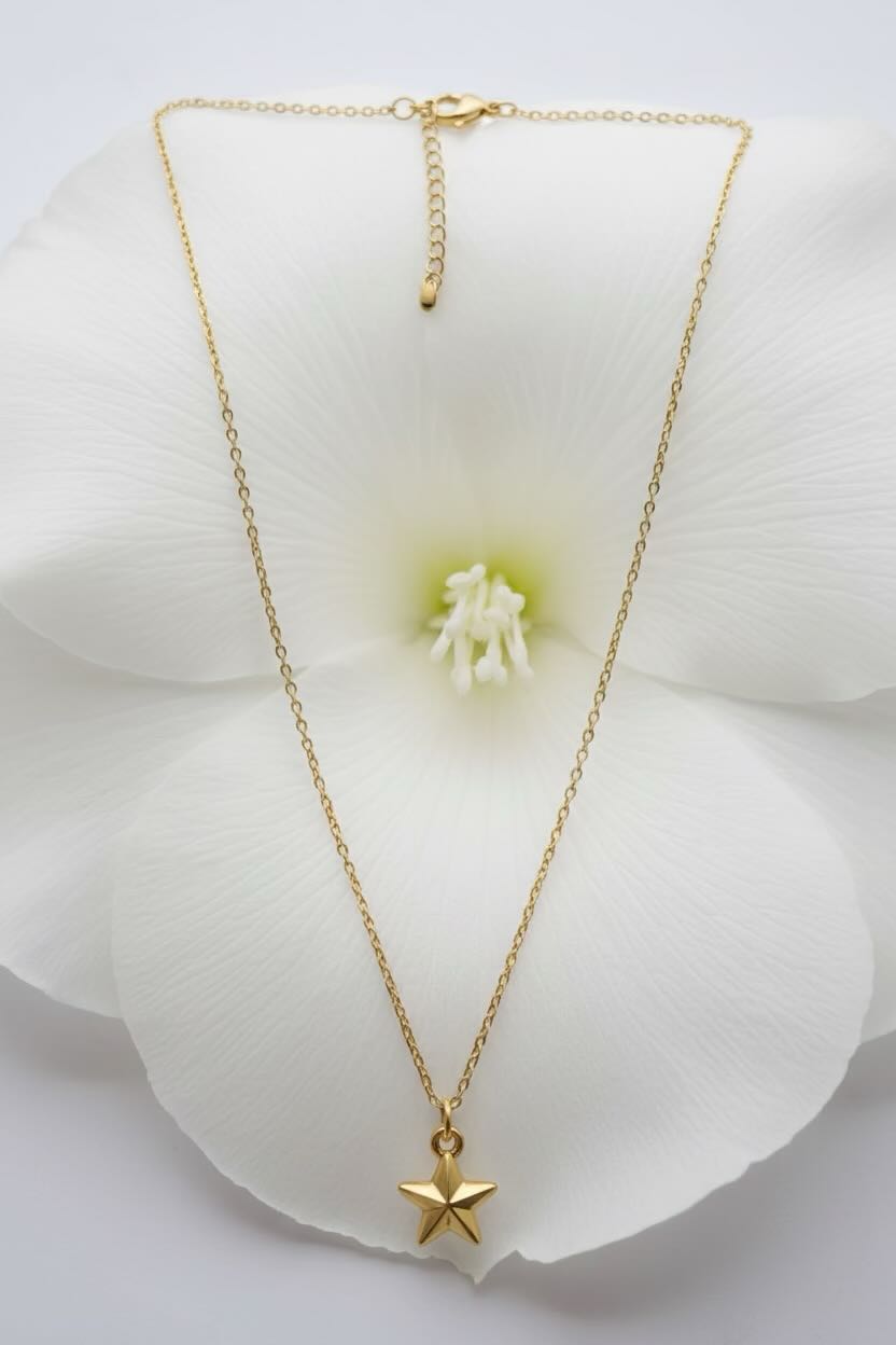 A delicate gold necklace with a small five-pointed star pendant, displayed on the white petals of a large flower.