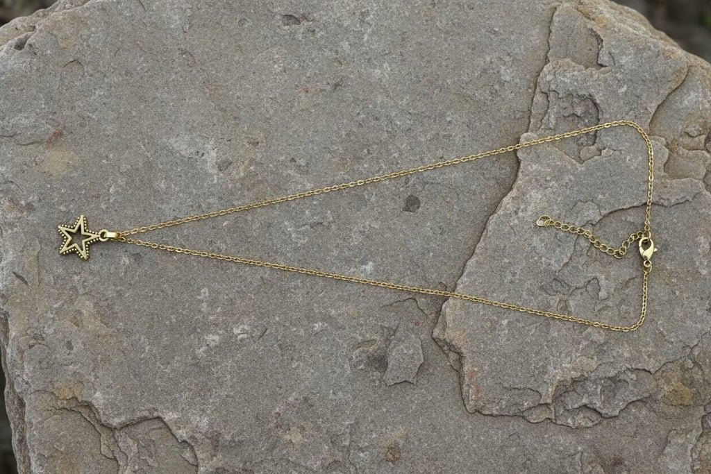A delicate gold chain necklace with a small star-shaped pendant, laid out on a textured gray stone surface.
