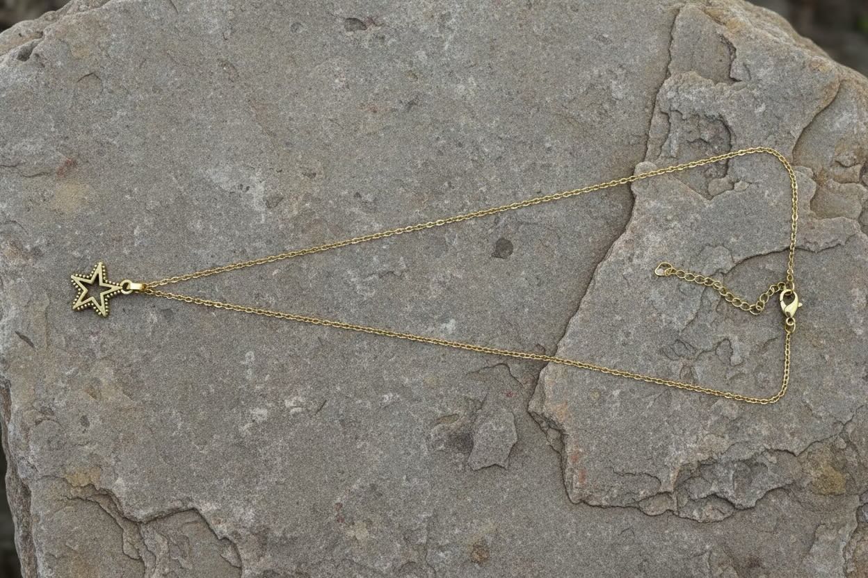 A delicate gold chain necklace with a small star-shaped pendant, laid out on a textured gray stone surface.