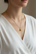 A close-up of a model wearing a delicate gold chain necklace with a small star-shaped pendant, styled with a white V-neck top.