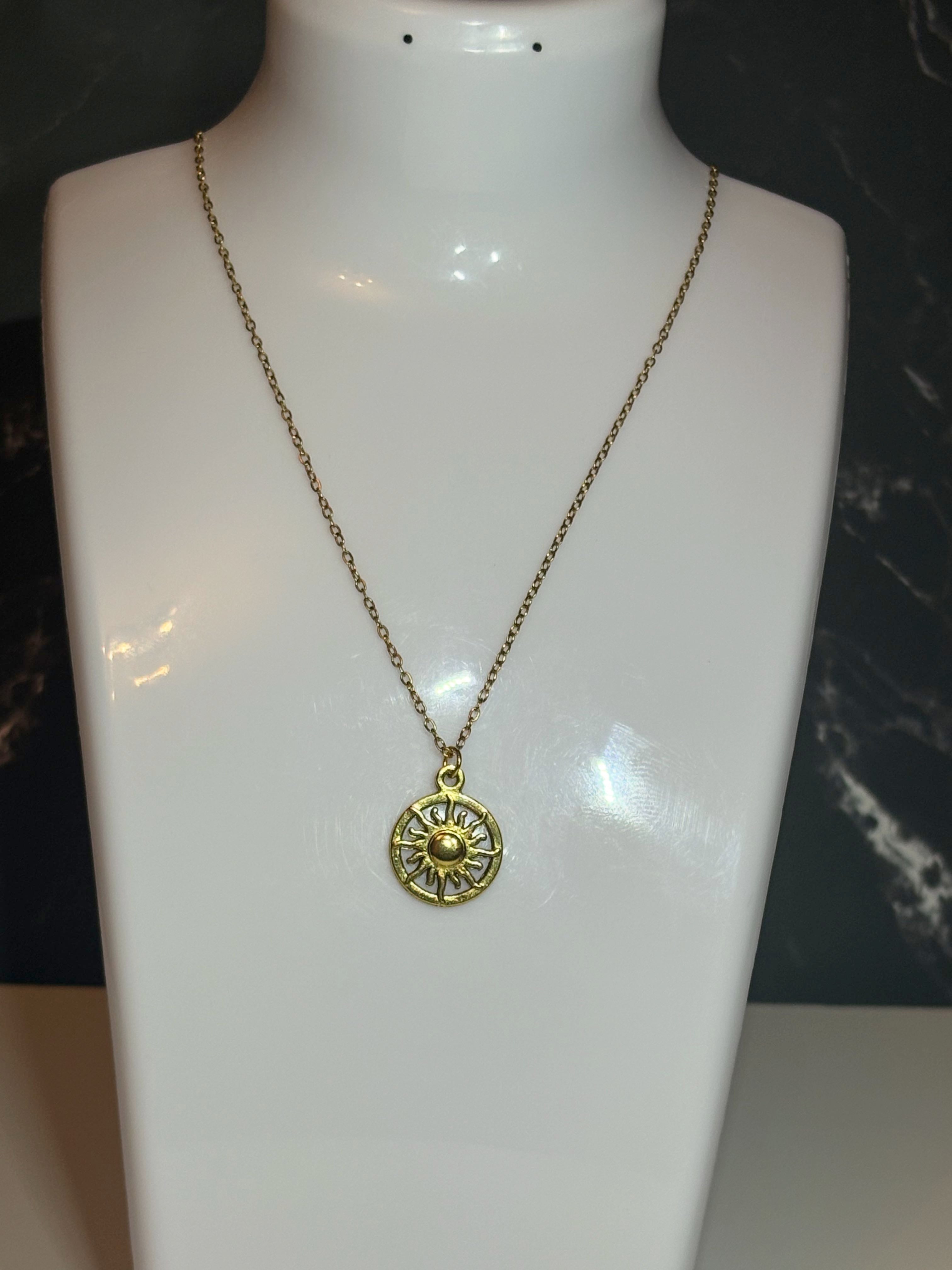 A gold-toned necklace with a circular sunburst pendant displayed on a white mannequin bust against a dark background.