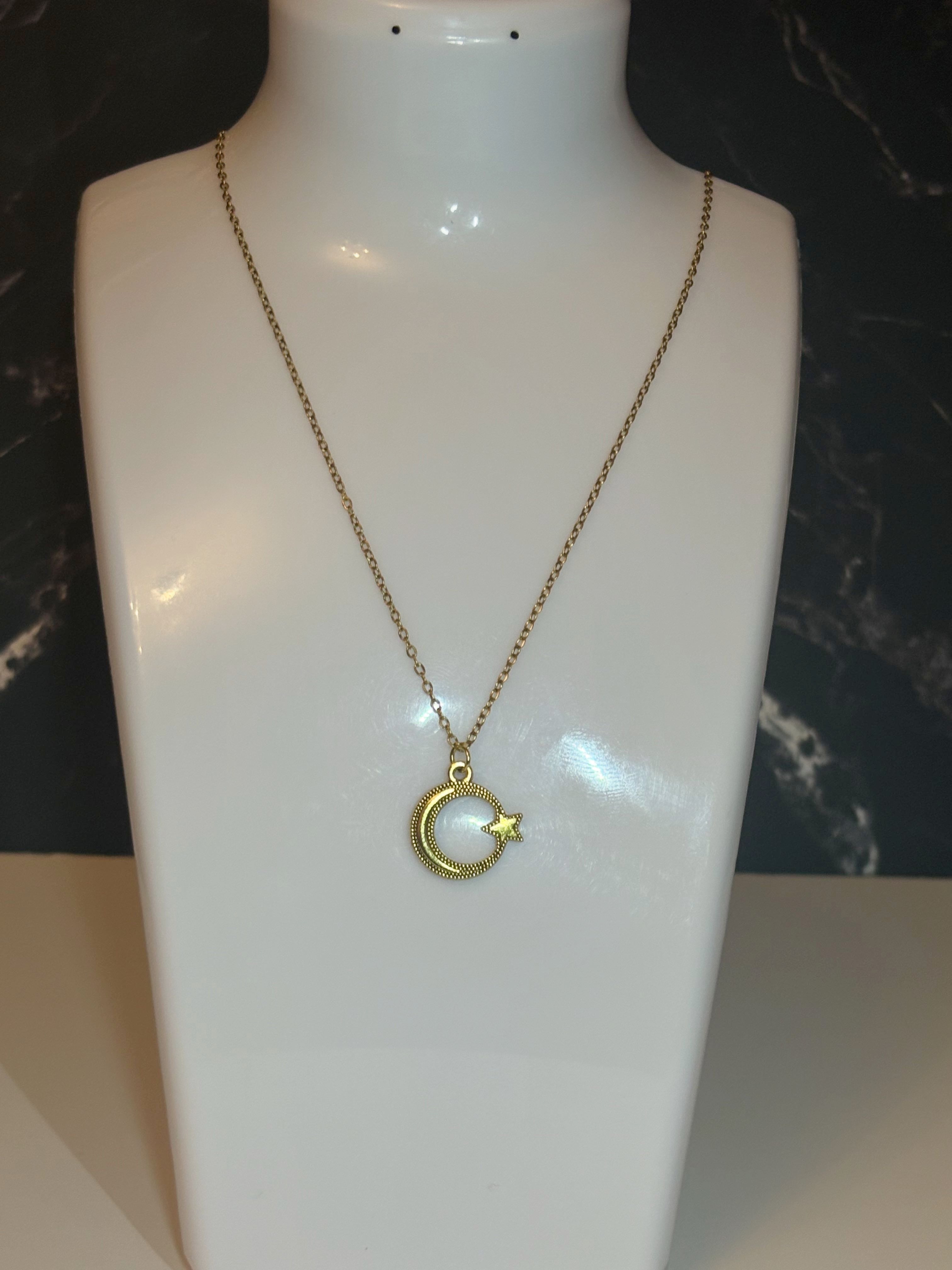 A gold crescent moon and star pendant necklace displayed on a white mannequin bust against a dark marble-patterned background.