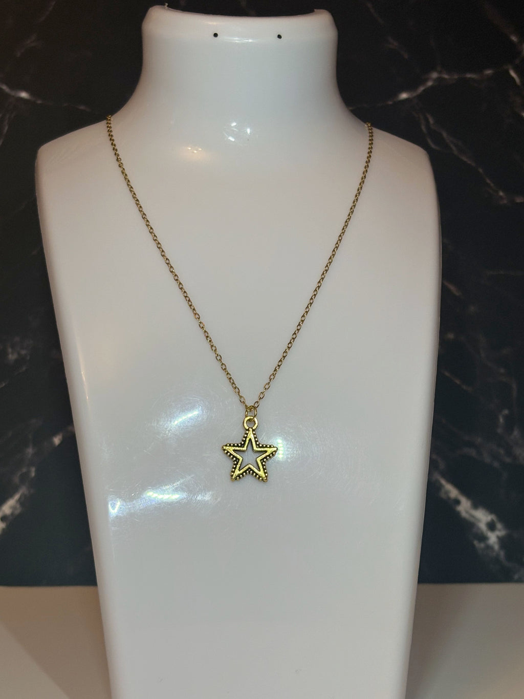 A gold star pendant necklace displayed on a white mannequin bust against a dark marble-patterned background.