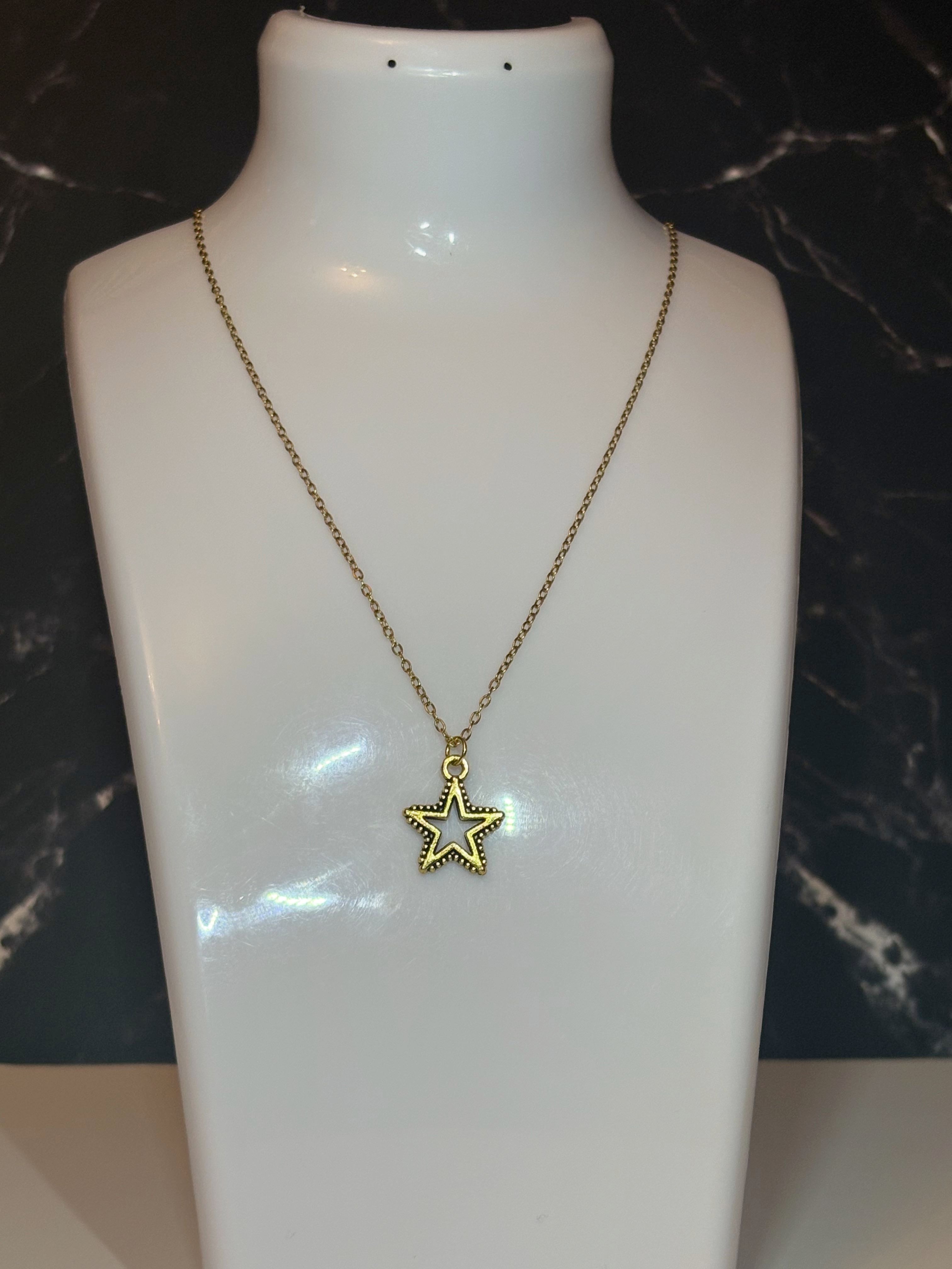 A gold star pendant necklace displayed on a white mannequin bust against a dark marble-patterned background.