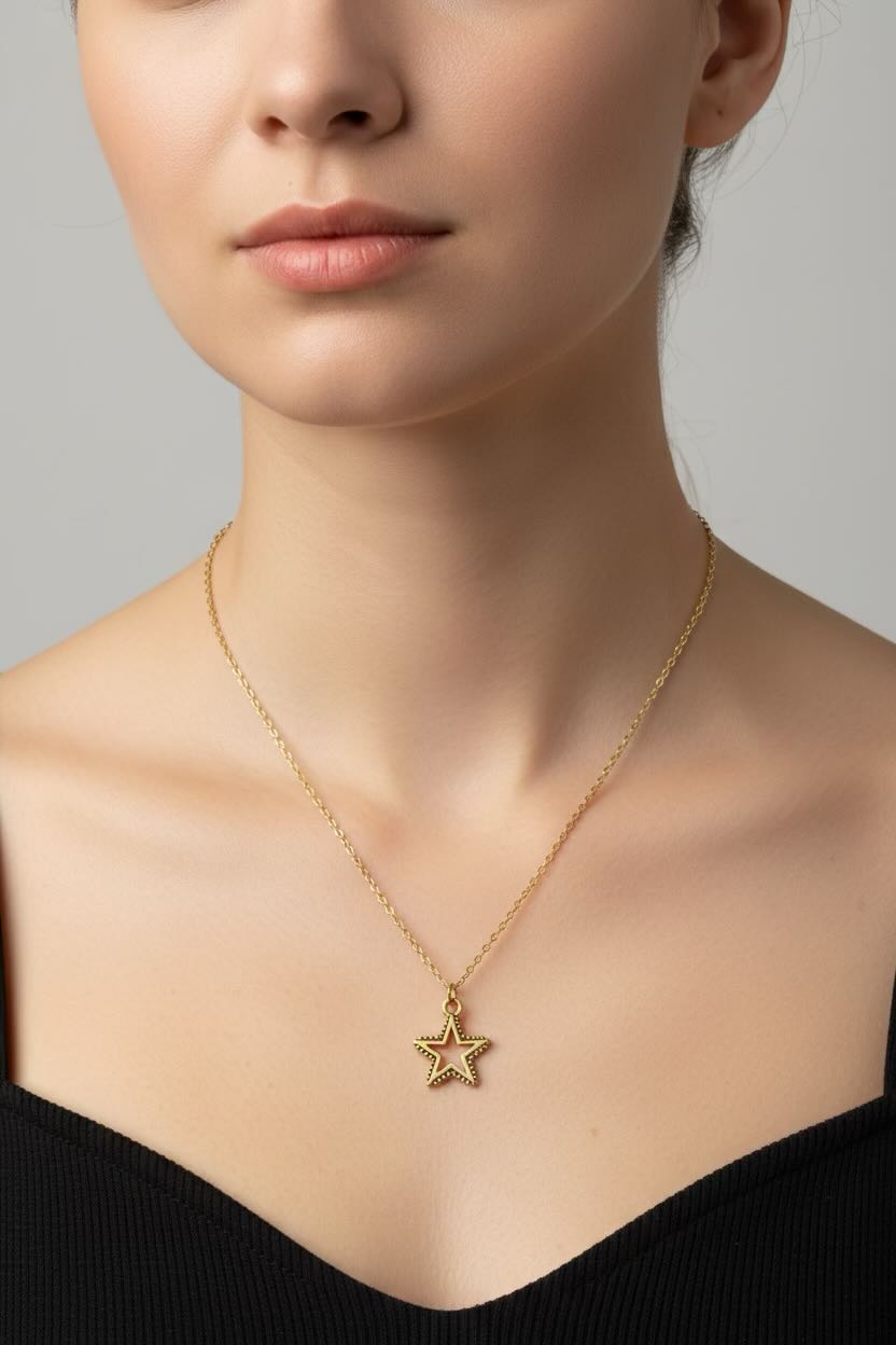 A close-up of a model wearing a delicate gold chain necklace with a small, star-shaped pendant against a neutral gray background.