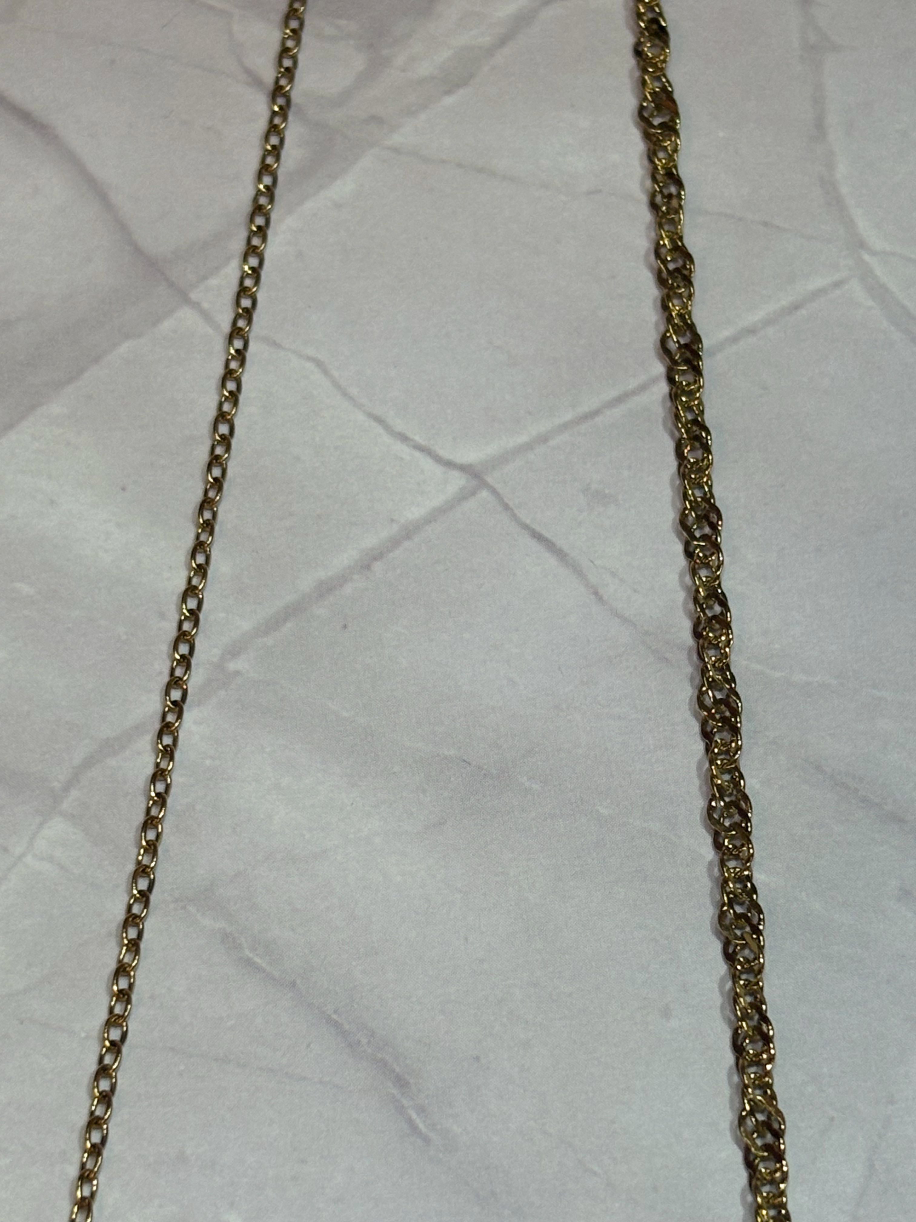 A close-up of a gold-toned chain and water wave chains laid flat on a wrinkled white paper background.