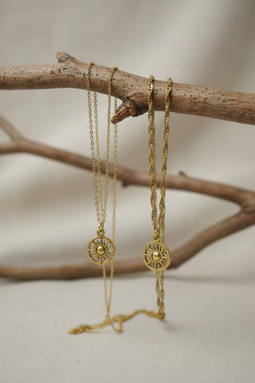 Two gold-toned chain necklaces with circular sunburst pendant charms, displayed on a plain light gray background.