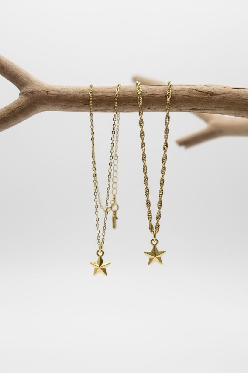 Two gold-tone layered necklaces with star pendants hanging from a natural driftwood branch against a light gray background.