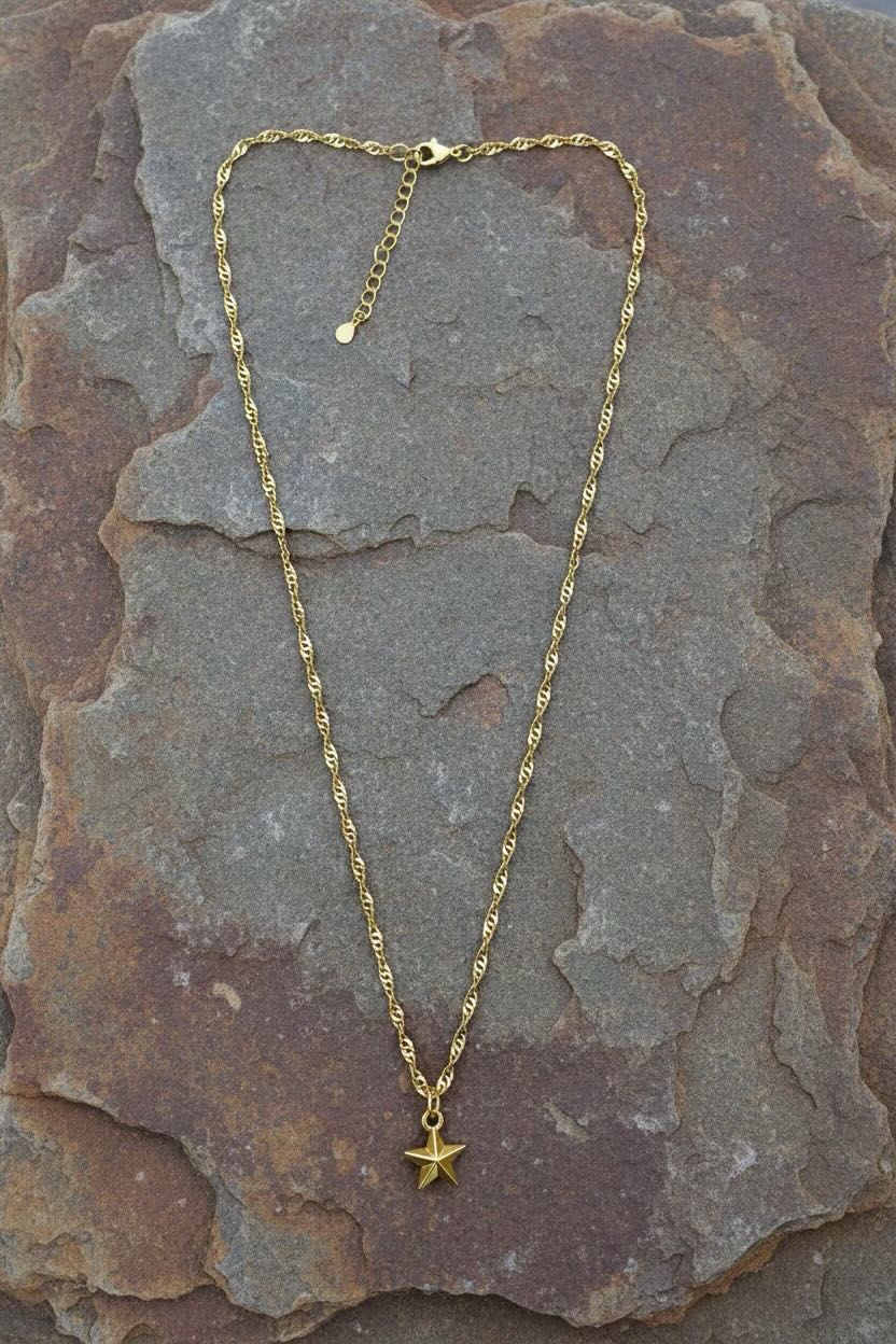 A gold rope chain necklace with a small star-shaped pendant, displayed on a textured brown and gray stone surface.