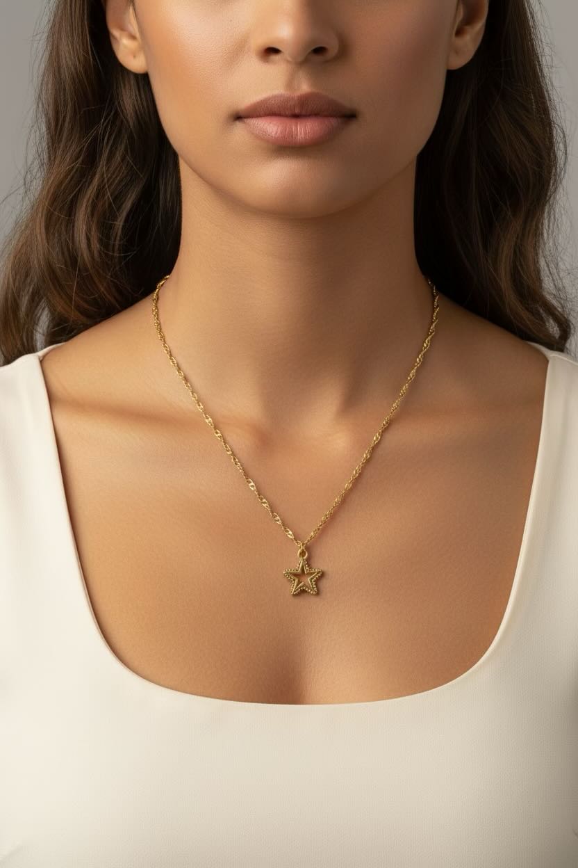 A close-up of a model wearing a delicate gold chain necklace with a small star-shaped pendant, paired with a white scoop-neck top.