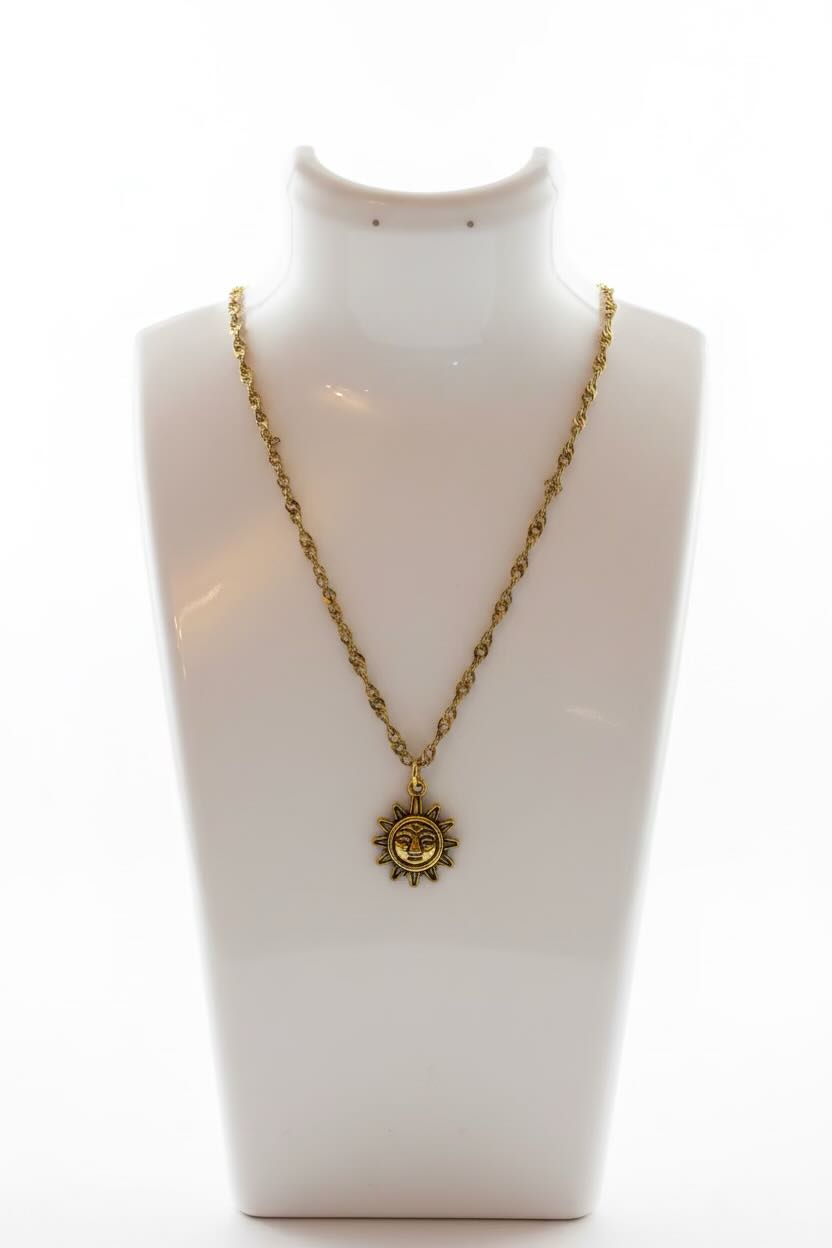 A gold chain necklace with a circular sun face pendant displayed on a white jewelry bust against a white background.