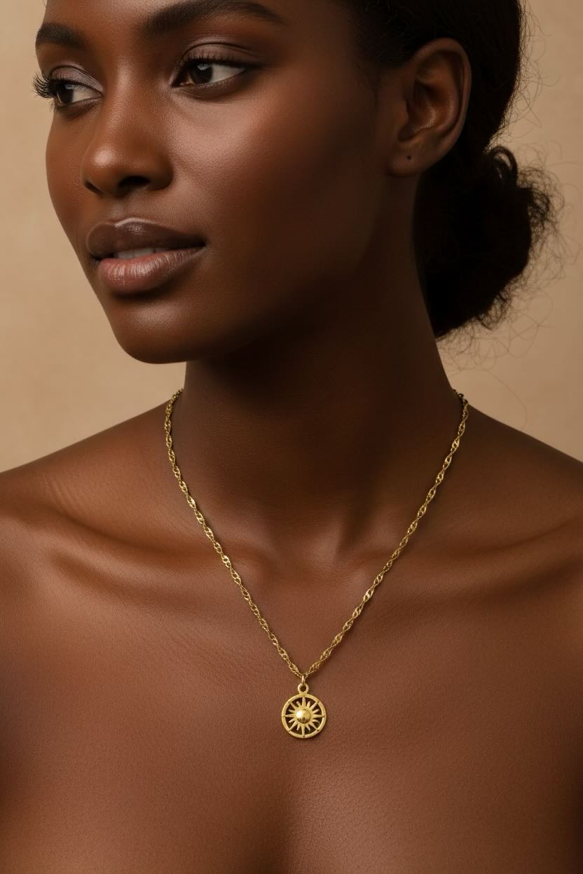 A close-up of a woman wearing a delicate gold chain necklace with a circular sunburst pendant, set against a warm beige background.