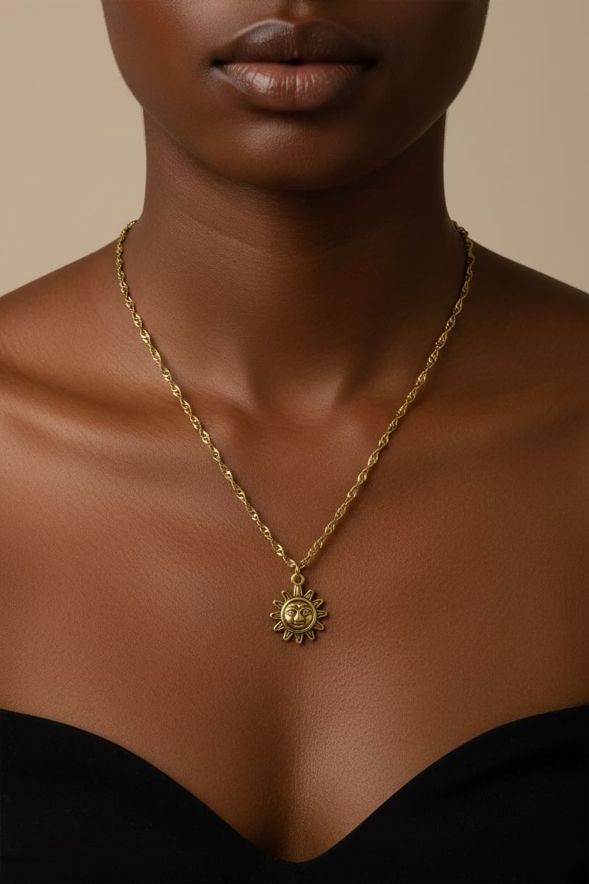 A gold necklace with a sun face pendant worn by a model, shown from the chest up against a warm beige background.