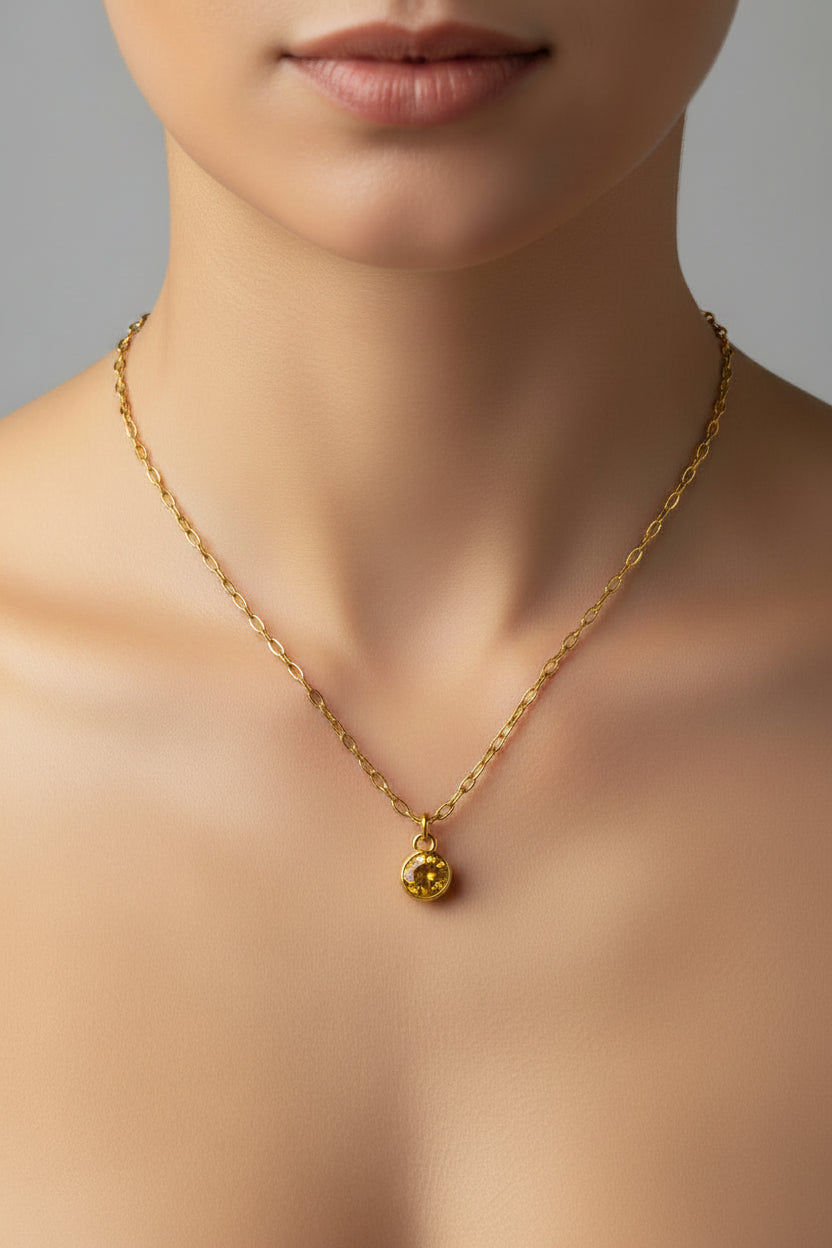 A close-up of a model's neck and upper chest wearing a delicate gold chain necklace with a small gold pendant.
