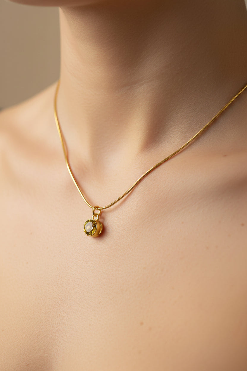 A delicate gold chain necklace with a small oval pendant featuring a yellow-green stone, shown worn on a model's neck.