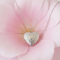 Silver heart-shaped locket necklace on a large petal