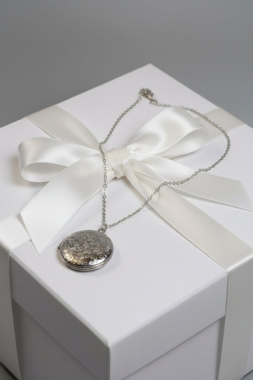 Silver necklace with a round patterned locket on a large gift box.