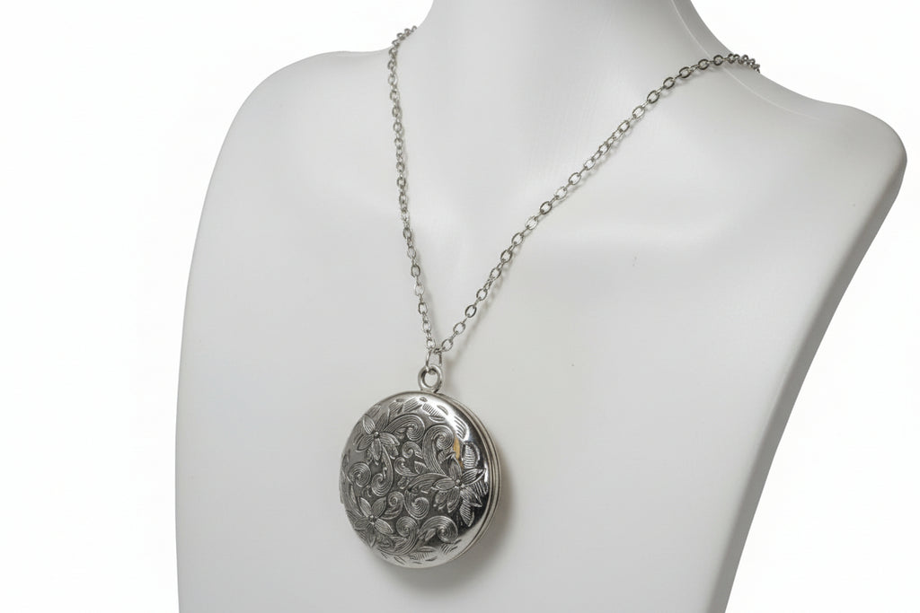 Silver necklace with a round patterned locket on a mannequin bust.