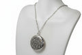 Silver necklace with a round patterned locket on a mannequin bust.
