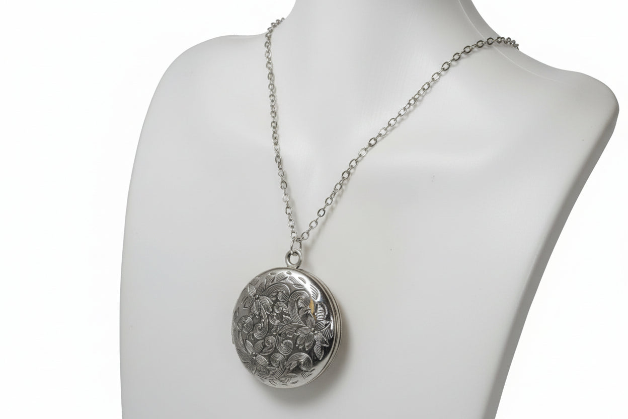 Silver necklace with a round patterned locket on a mannequin bust.