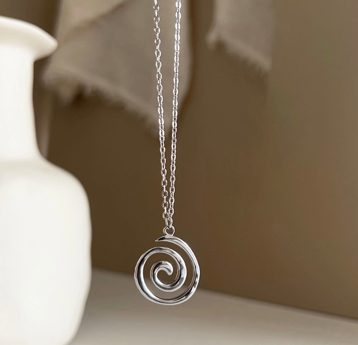 Silver spiral pendant necklace on a neutral background