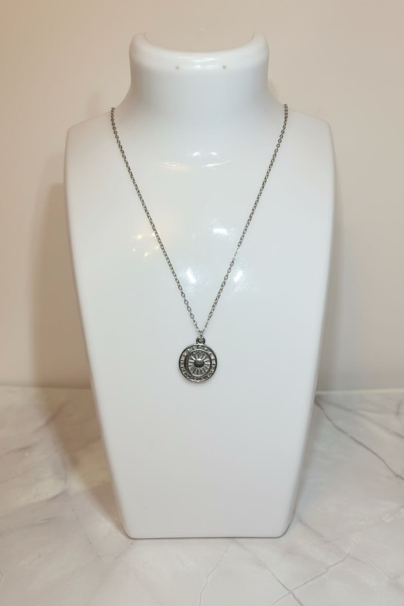A silver pendant necklace displayed on a white jewelry bust against a light beige background.
