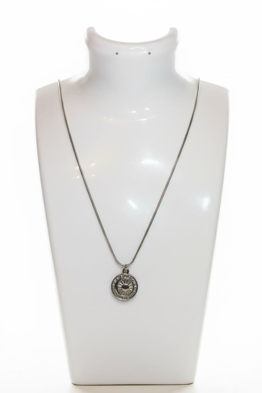 A silver-toned necklace with a circular pendant displayed on a white neck mannequin against a white background.
