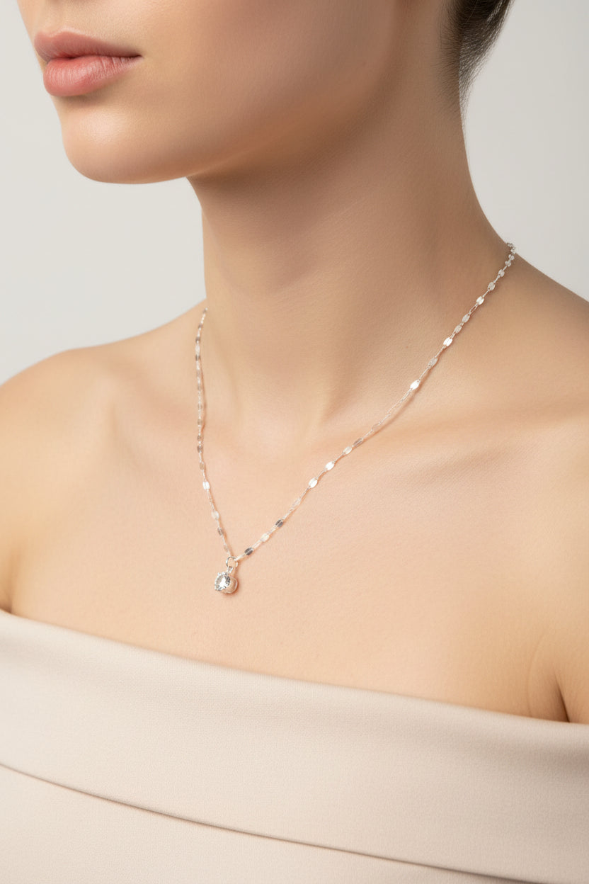 A silver-toned beaded necklace with a small clear teardrop crystal pendant, displayed on a model