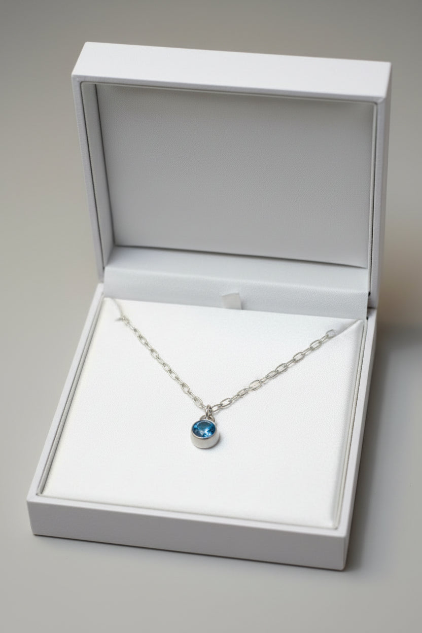 Necklace with a blue birthstone pendant in a gift box.
