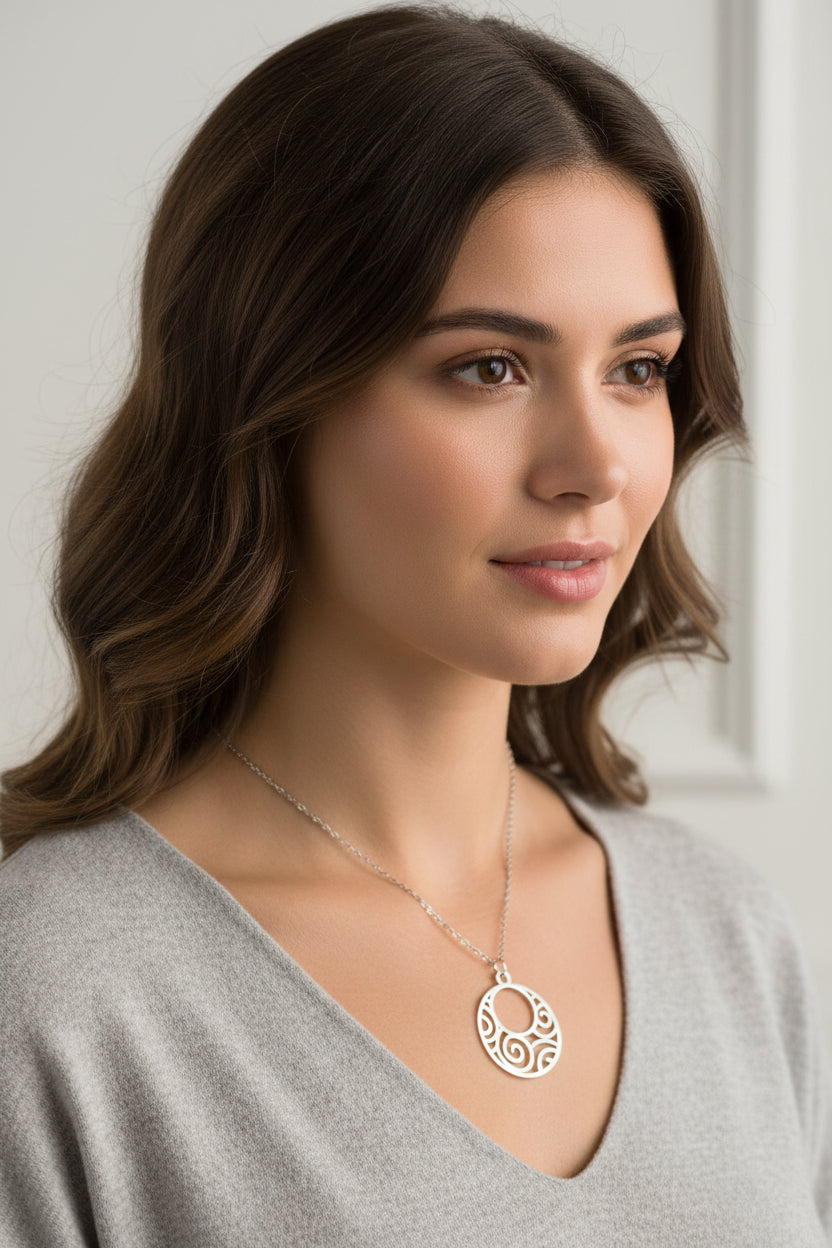A silver necklace with a circular pendant featuring swirl cutouts, displayed on a model.