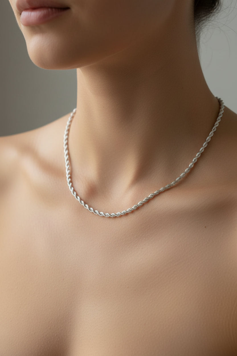A silver-toned chain necklace with a small decorative clasp, laid flat on a light gray marble-patterned surface.