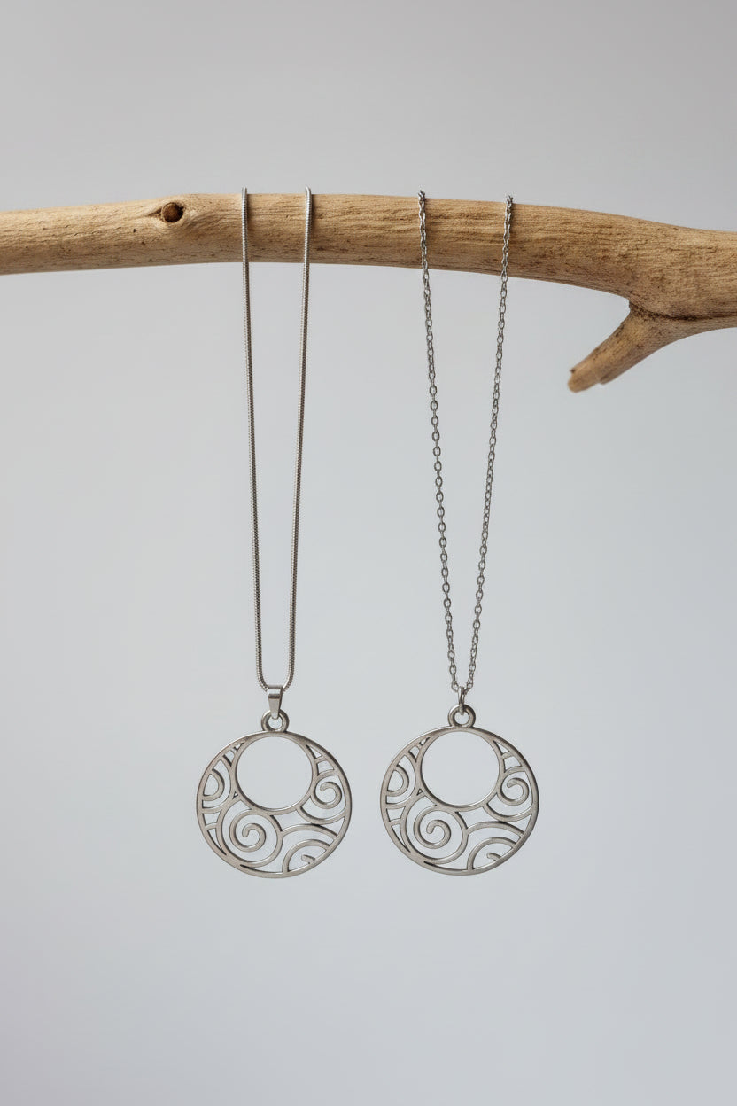 Two silver-tone circular pendant necklaces with openwork swirl patterns, displayed on a plain light background.