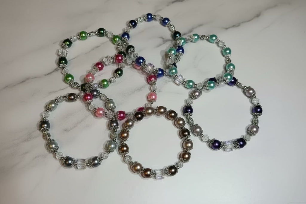 Seven beaded stretch bracelets with glass pearl round beads in various colors, arranged on a white marble surface.