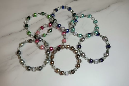 Seven beaded stretch bracelets with glass pearl round beads in various colors, arranged on a white marble surface.