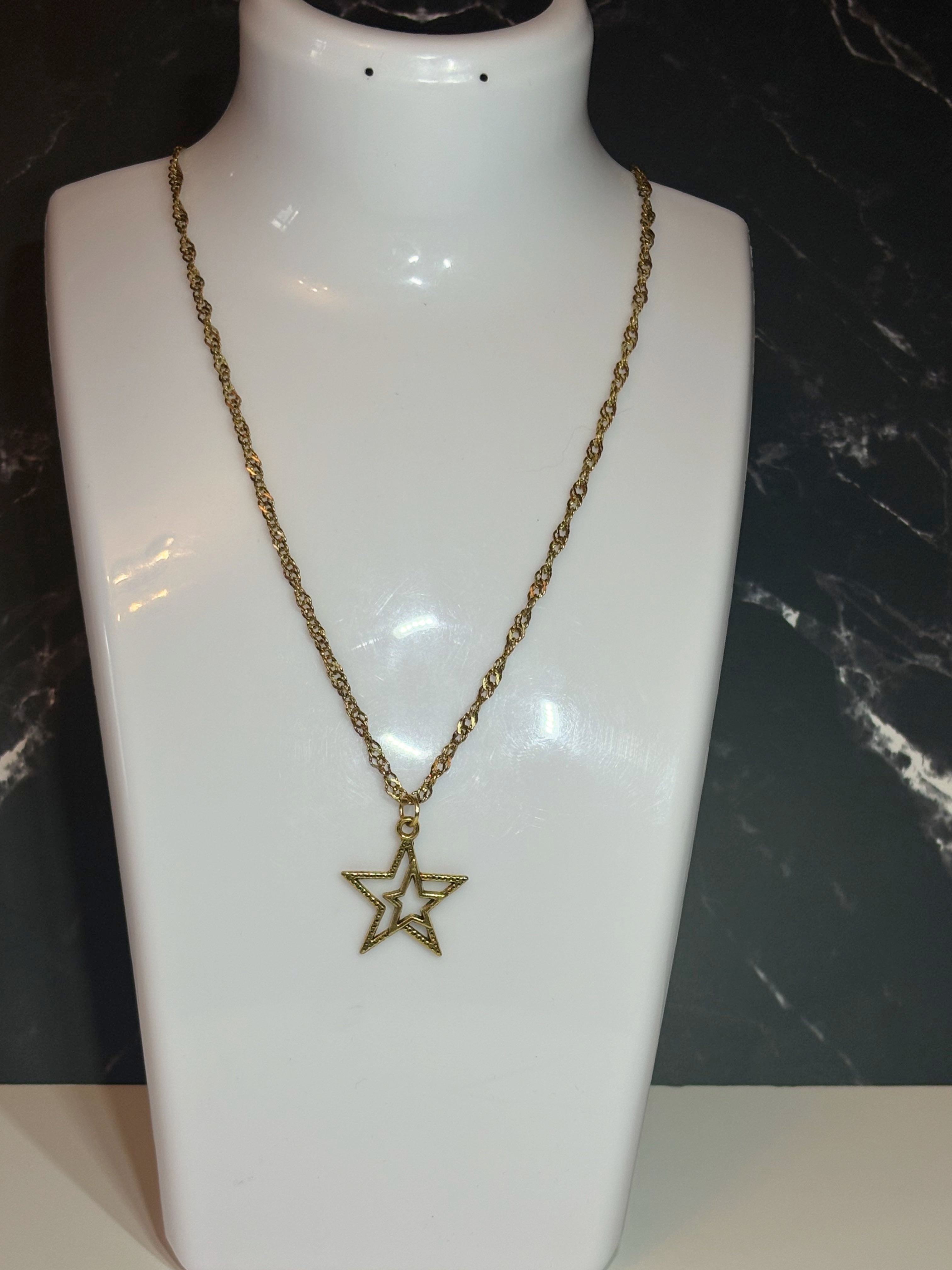 A gold-toned chain necklace with an open star-shaped pendant, displayed on a white jewelry bust against a dark marble-patterned background.
