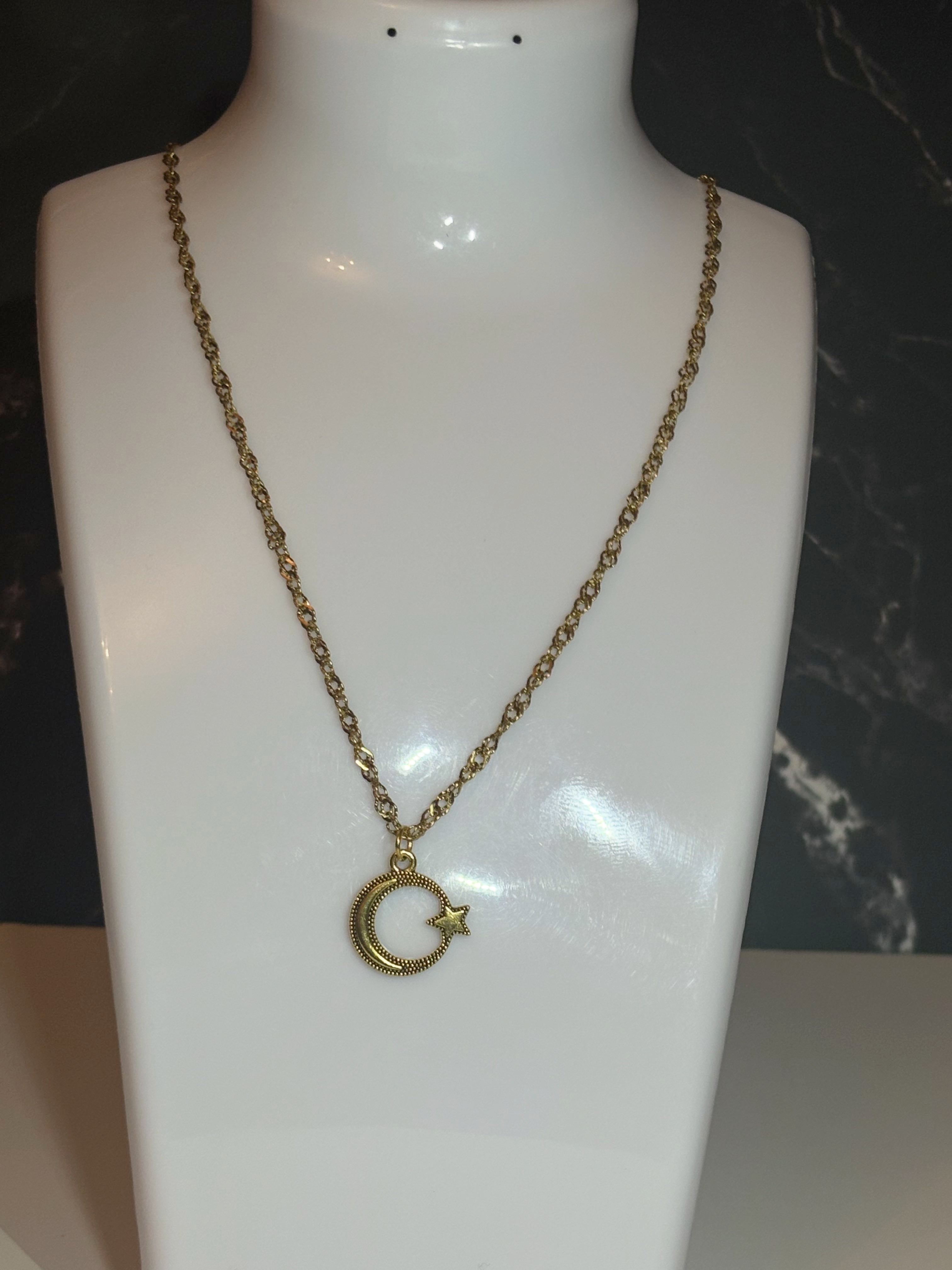 A gold-toned chain necklace with a crescent moon and star pendant, displayed on a white mannequin bust against a dark background.