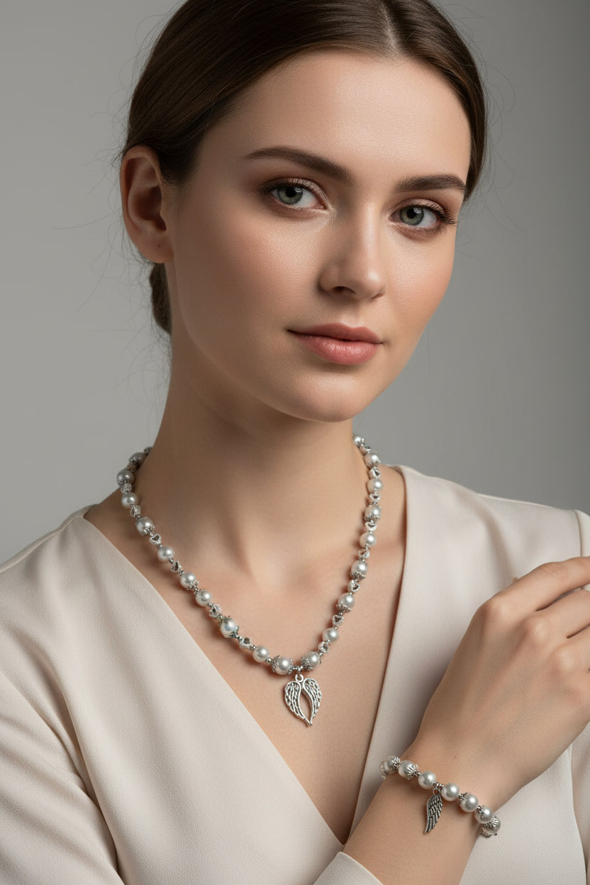 A silver-toned jewelry set featuring a long white pearl necklace and a matching pearl bracelet, both with metallic bead details and a small wing-shaped charms, displayed on a plain light background.